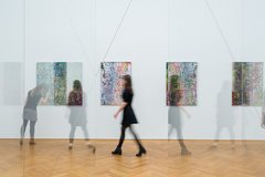 Besucher laufen durch Ausstellung und betrachten Gemälde