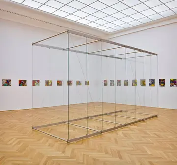 Ausstellungsraum mit einer Reihe kleiner quadratischer Werke an der Wand und in der Mitte Glasscheiben