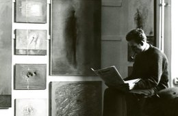 Wand mit Bildern von Gerhard Richter während des Akademierundgangs, Düsseldorf, im Februar 1962 (rechts im Bild Manfred Kuttner) Ein altes Foto, auf dem ein Mann mit einer Pfeife eine Zeitung liest und neben ihm Gemälde hängen