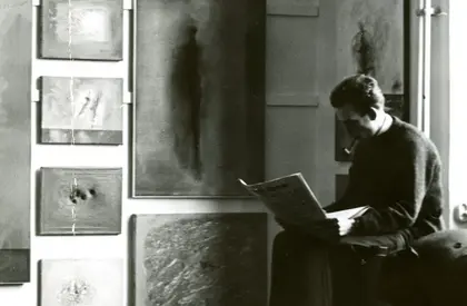 Wand mit Bildern von Gerhard Richter während des Akademierundgangs, Düsseldorf, im Februar 1962 (rechts im Bild Manfred Kuttner) Ein altes Foto, auf dem ein Mann mit einer Pfeife eine Zeitung liest und neben ihm Gemälde hängen